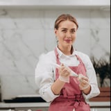 A woman wearing a pink apron is cutting a cake.