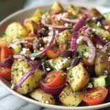 A bowl of vegetables with onions, tomatoes, potatoes, and cucumbers.