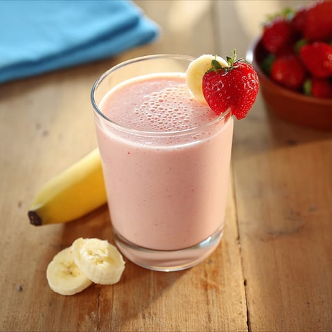 A glass of strawberry banana smoothie with a banana and strawberry on top.
