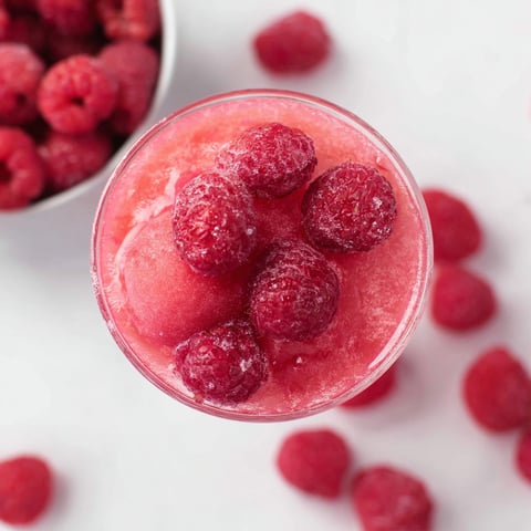 A glass of pink juice with raspberries in it.
