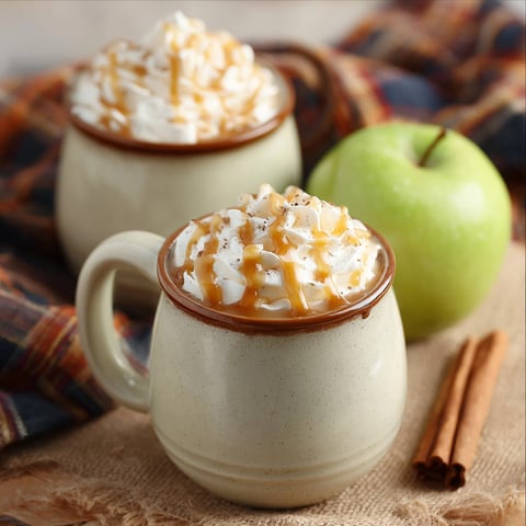 Two cups of cinnamon flavored coffee with a slice of apple.