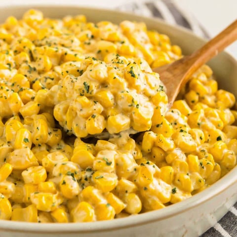 A bowl of corn with a wooden spoon in it.
