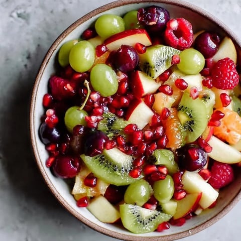 A bowl of fruit with kiwi, grapes, and pomegranate.