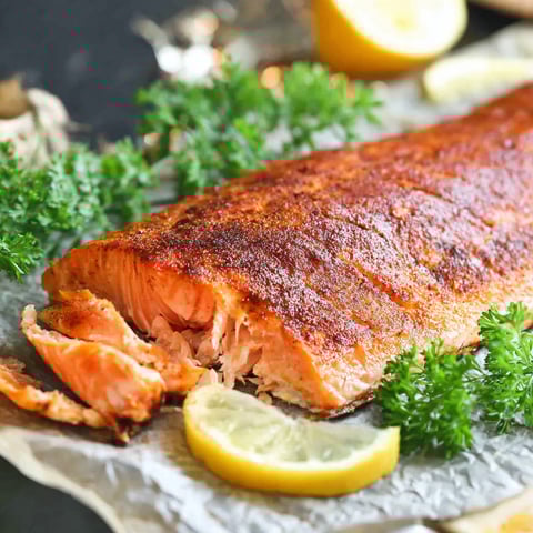 A fish on a cutting board with lemon wedges.